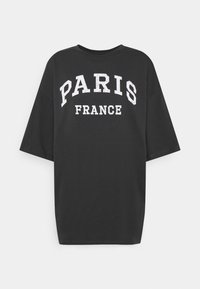 Camiseta negra de gran tamaño con mangas cortas, que presenta una impresión blanca de "PARÍS" y "FRANCIA" en una fuente negrita y desgastada.