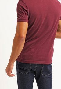 Burgundyröd kortärmad t-shirt i en figurnära passform, med mjuk textur och diskret stretch, parat med mörk denim-jeans med bakfickor.