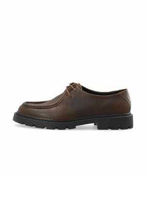Brauner Leder-Schnürschuh mit dicker schwarzer Gummisohle und abgerundetem quadratischem Zehenbereich, von der Seite auf weißem Hintergrund dargestellt.