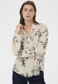Beige bluse med sort botanisk tryk, med en klipkrave, lange ærmer og en afslappet pasform. Fremstillet af letvægtsstof.