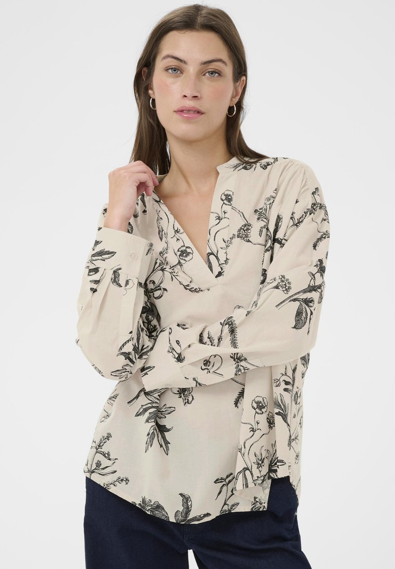 Beige bluse med sort botanisk tryk, med en klipkrave, lange ærmer og en afslappet pasform. Fremstillet af letvægtsstof.