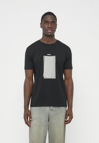 Čierne tričko s krátkym rukávom s strieborným grafickým dizajnom obsahujúcim zvislé čiary a logo "BOSS" nad dizajnom. Bavlnená tkanina, bežný strih.