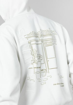 Sweat à capuche blanc avec un motif crème représentant l'entrée d'un café avec un panneau "OUVERT", des plantes et des détails floraux, texte en relief sur le côté.