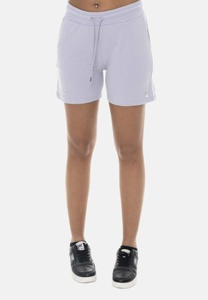 Femme portant un short violet clair à cordon de serrage et des baskets noires, debout avec les jambes visibles de la taille aux pieds sur fond blanc.