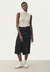 Czarna spódnica midi z kordurowego materiału z rozcięciem z przodu, w połączeniu z beżowym topem bez rękawów i białymi sneakersami. Prosty design z delikatną teksturą.