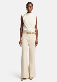 Un haut sans manches beige associé à un pantalon large crème taille haute, rehaussé d'une ceinture beige clair et de chaussures à talons jaunes texturées.