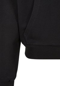 Hoodie noir avec un tissu texturé, des poignets côtelés et une poche kangourou. Le design est simple avec des lignes épurées et une coupe ajustée.