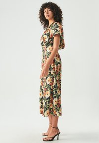 Gėlių suknelė trumpomis rankovėmis; juodas pagrindas su geltonomis ir raudonomis gėlėmis; vidutinio ilgio su prigludusia juosmena; derinama su juodais dirželių kulniukais.