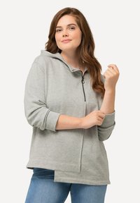 Felpa grigia con cappuccio, con zip, maniche a tre quarti, vestibilità rilassata e tessuto strutturato. Dettaglio della zip visibile sul davanti.
