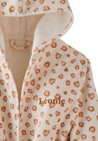 Fleece-Haube mit einer cremefarbenen Basis, die mit rosa und braunen Herzmustern verziert ist. Gestickter Name "Léonie" in orangefarbenem Faden in der Nähe des Reißverschlusses.