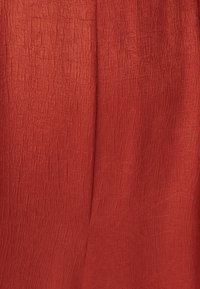 Raudona, tekstūruota medžiaga su raukšlėtu paviršiumi, turinti švelnias linijas ir matinį apdailą.