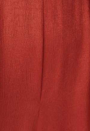 Tela roja, texturizada con una apariencia arrugada, que presenta líneas suaves y un acabado mate.