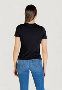 Camiseta negra de algodón con mangas cortas y cuello redondo, combinada con jeans azules ajustados que presentan bolsillos traseros y un sutil detalle de costura.