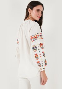 Witte blouse met kleurrijke bloemenborduursels op de mouwen, geplooide mouwen en een ontspannen pasvorm. Lichtgewicht stof met een gladde textuur.