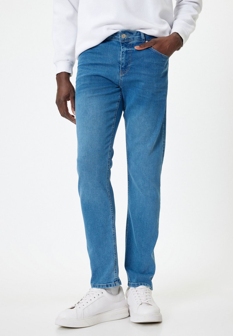 Jeans de mezclilla azul claro con corte recto, que cuentan con trabillas para cinturón, un cierre frontal con botón y bolsillos delanteros y traseros. Estilizados con zapatillas blancas.