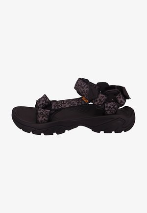 Sandalia exterior negra y gris con suela gruesa y correas estampadas ajustables, con un pequeño logo naranja "Teva" en la correa lateral.