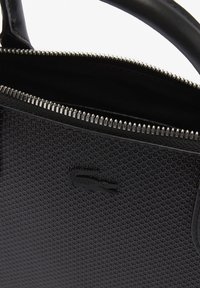 Czarna torebka o fakturze, z zamkiem błyskawicznym, srebrnymi elementami i wytłoczonym logo. Gładka rączka dopełnia design.