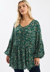Blusa floreale verde con maniche lunghe a sbuffo e scollatura a girocollo. Il tessuto presenta delicati motivi floreali dorati e un design fluido e arricciato.