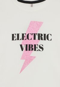 Vit t-shirt med en stor rosa glittrig blixt och fet svart text som säger "ELECTRIC VIBES." Rund hals.
