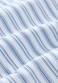 Baumwollstoff mit einem wellenförmigen Muster aus blauen und navyblauen Streifen auf einem weißen Hintergrund, der eine glatte Textur und einen weichen Abschluss präsentiert.