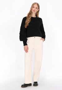 Czarny sweter o fakturze z obszernymi rękawami, zestawiony z kremowymi spodniami typu wide-leg i czarnymi butami na platformie. Prosty i nowoczesny design.