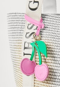 Sac fourre-tout tissé blanc et gris, orné d'un porte-clés en caoutchouc rose représentant une cerise avec des feuilles vertes, maintenu par une sangle rose et des éléments en métal doré.