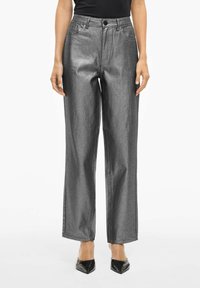 Pantalones de pierna ancha de color gris metálico con una textura suave, que presentan un cierre de botón en la parte frontal y bolsillos laterales. Combinados con tacones negros de punta.