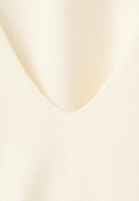 Jersey de punto color crema con un tejido suave y texturizado. Presenta un sutil acanalado en el escote en forma de V, creando un diseño limpio y minimalista.