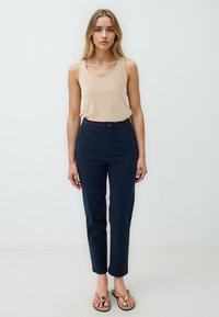 Top beige, pantaloni blu navy a vita alta e infradito color sabbia. I pantaloni sono aderenti, con chiusura a bottone e design a gamba dritta.