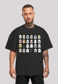 Sort T-shirt med et gitter af 30 forskelligartede hjelmdesigns i hvid, gul, blå, grøn og rød mod stoffet. 100% bomuldsstof, løs pasform.