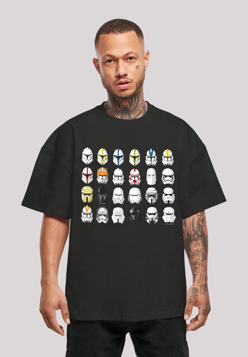 Sort T-shirt med et gitter af 30 forskelligartede hjelmdesigns i hvid, gul, blå, grøn og rød mod stoffet. 100% bomuldsstof, løs pasform.