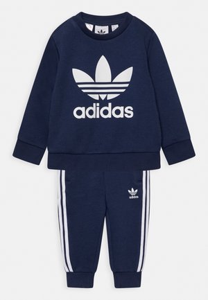 Tuta Adidas blu navy con felpa a maniche lunghe caratterizzata da un logo bianco e pantaloni abbinati con strisce laterali bianche e tasche.