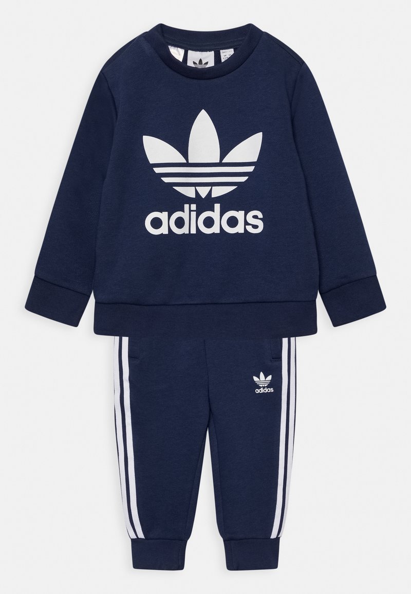 Trening Adidas de culoare albastru marin, cu hanorac cu mânecă lungă, având un logo alb și pantaloni asortați cu dungi albe pe lateral și buzunare.