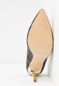 Chaussure à talon haut à bout pointu avec tige marron à motif, semelle beige embossée du logo "GUESS" et talon stiletto métallique doré.