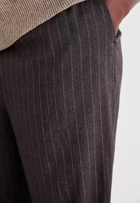Dark gray tailored pants with a fine pinstripe pattern, featuring a smooth texture and a structured fit. Includes a side pocket detail.