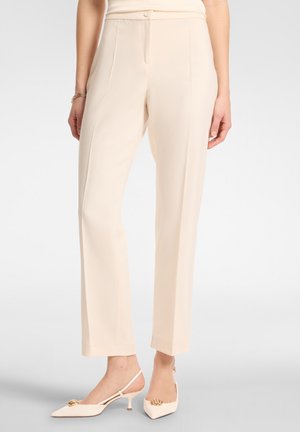 Pantaloni beige chiaro su misura in tessuto morbido, con chiusura a bottone, davanti piatto e gambe dritte, abbinati a eleganti décolleté bianche con tacco.