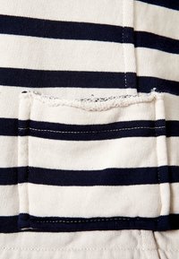 Tejido a rayas en colores navy y blanco; bolsillo prominente con bordes deshilachados; textura de algodón ligero. Costuras visibles en los bordes.