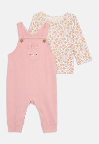 Pink ribbed overalls with a bunny pocket, wooden buttons, and snap closures. Accompanied by a white long-sleeve shirt with floral patterns.