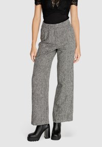 Pantaloni larghi grigi, texture, con vita alta e fascia elastica. Abbinati a stivali platform neri.