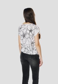 Balts īsroku tops ar melnu ziedu kontūru rakstu, savienots ar tumšām džinsu biksēm. Topam ir apaļa kakla izgriezums un nedaudz pieplešams apakšmala.