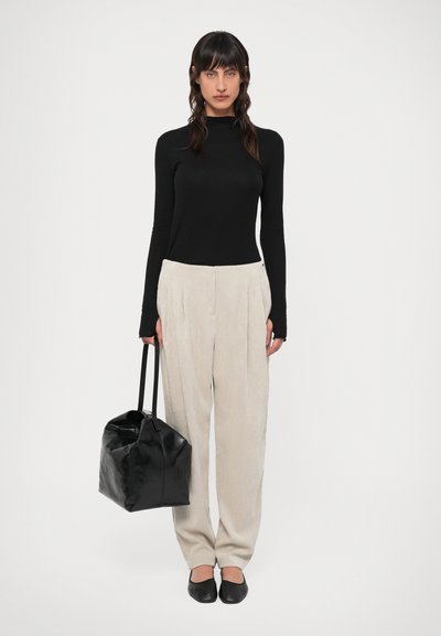 Juodas ilgomis rankovėmis viršus, smėlio spalvos klostuoti kelnių, juodi plokšti batai ir juoda bendro rankena. Lygūs tekstūros ir neutralios spalvos.