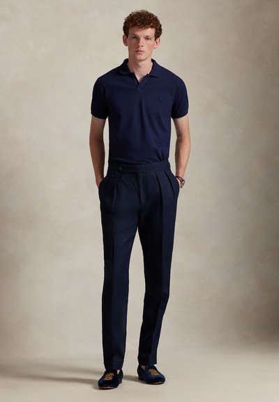 Navy polo shirt paired with pleated navy trousers. Fitted design, smooth fabric, and embroidered loafers with floral details.