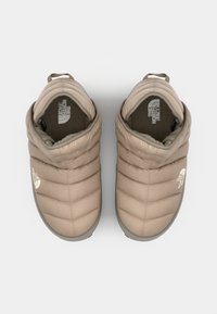 Chaussures rembourrées beiges avec une texture douce, une forme arrondie et un détail de logo. Comprend une languette pour un enfilage facile. Semelle antidérapante.