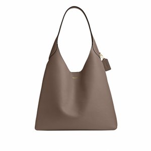 Sac à épaule en cuir marron avec une seule sangle, logo doré et étiquette de marque suspendue sur fond blanc.