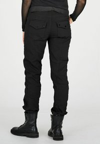 Person wearing black cargo pants with flap pockets and black lace-up combat boots, standing with one hand on hip.