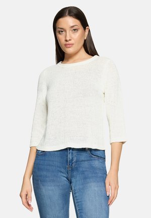 Pull blanc en maille avec un col rond, des manches trois-quarts et une coupe décontractée, associé à un jean bleu.