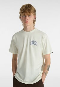 Cremefarvet kortærmet t-shirt lavet af bomuld, med et blåt grafisk design på venstre bryst. Løs pasform med rund halsudskæring.