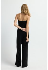 Mono negro sin tirantes con cuerpo ajustado y pantalones de pierna ancha, hecho de una tela suave con detalles de diseño mínimos.