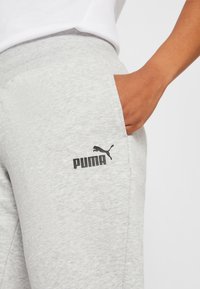 Grå bomulds sweatpants med ribbet talje, sidelommer og et sort Puma-logo på venstre lår. Glat tekstur, afslappet pasform.