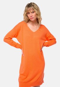 Robe en tricot orange à col en V, à manches longues, coupe décontractée et poignets côtelés. Sa texture douce et ses fentes latérales ajoutent un détail fonctionnel.